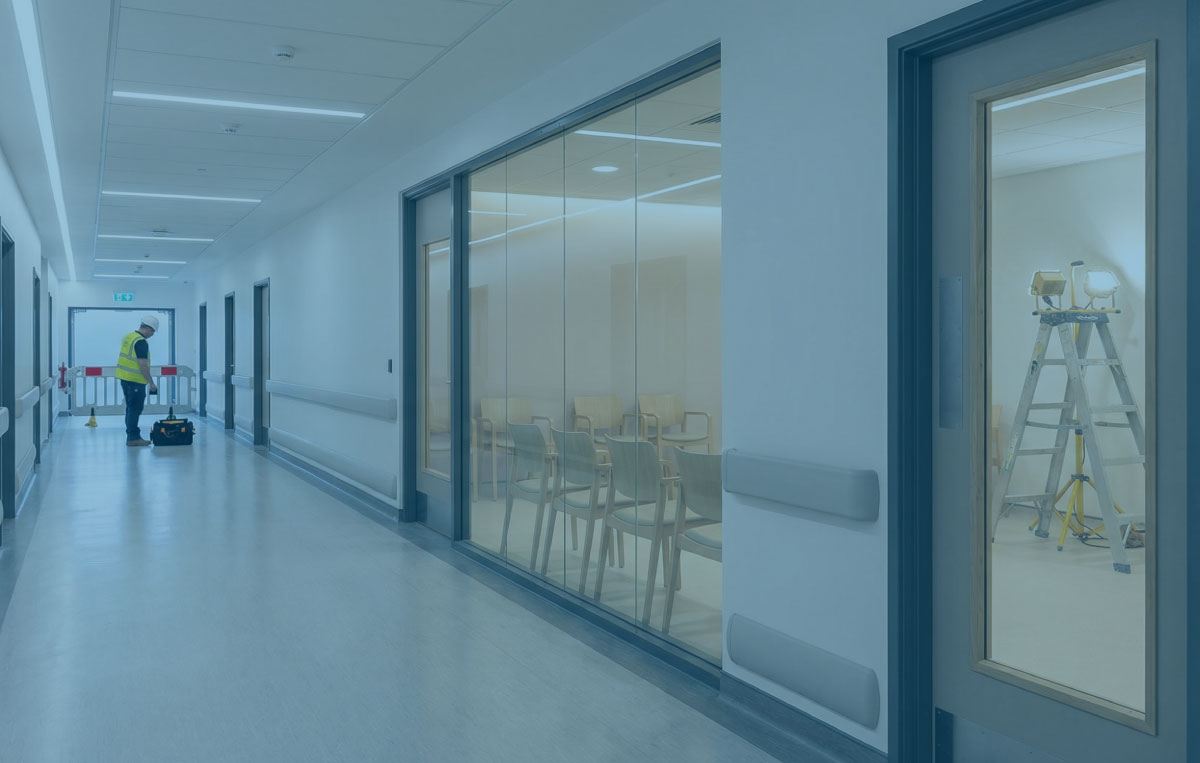 Healthcare corridor with a new clinic entrance and glazed waiting area, with subtle construction activity visible beyond