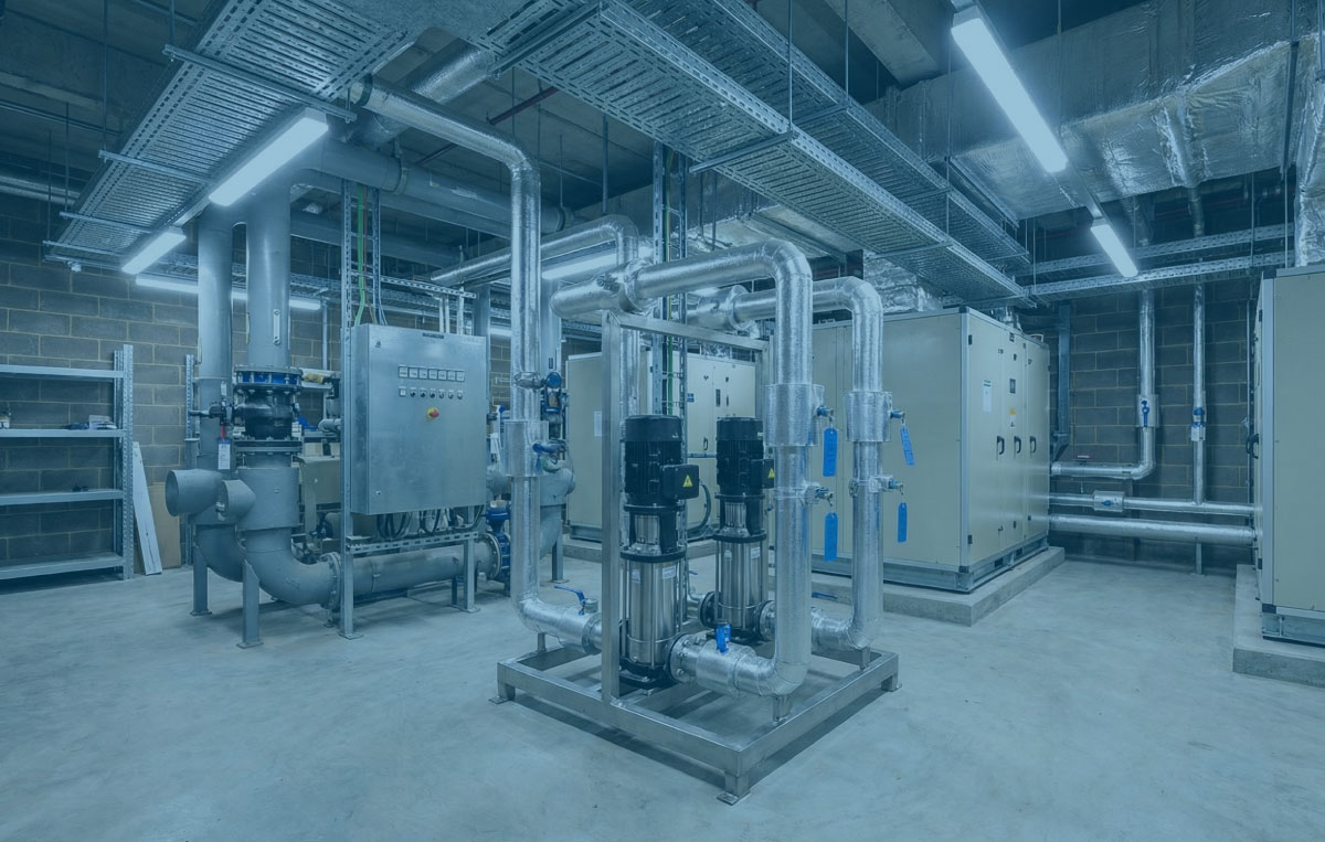 Real plant room with a central skid, new pipework and labelled panels under bright white lighting