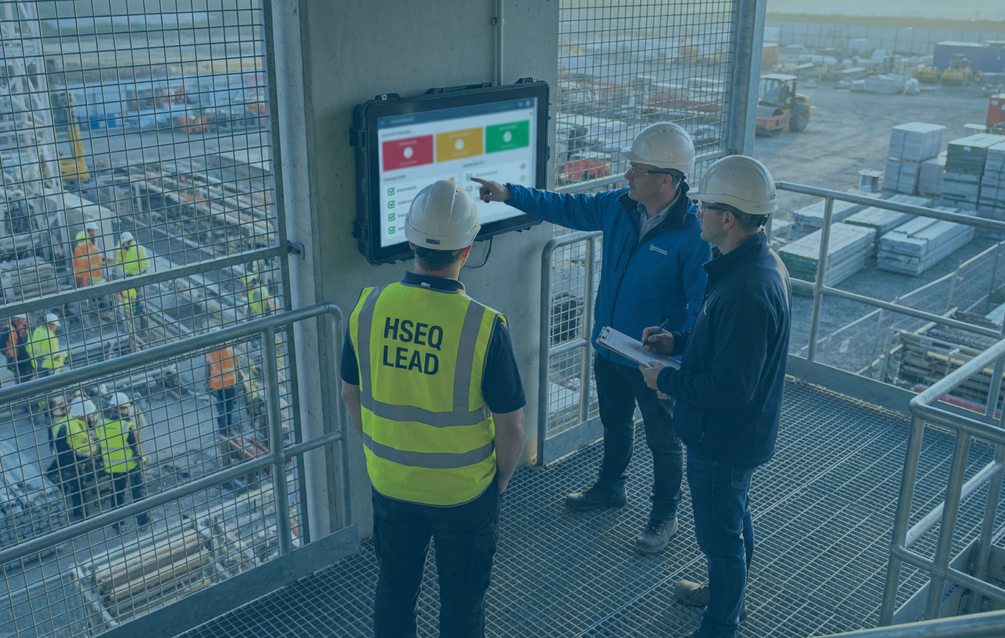 HSEQ lead and site team reviewing a digital safety and quality dashboard beside a live construction zone