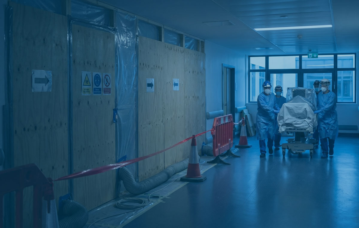Ward corridor at blue hour with sealed zone hoardings and a red route under clean work lights