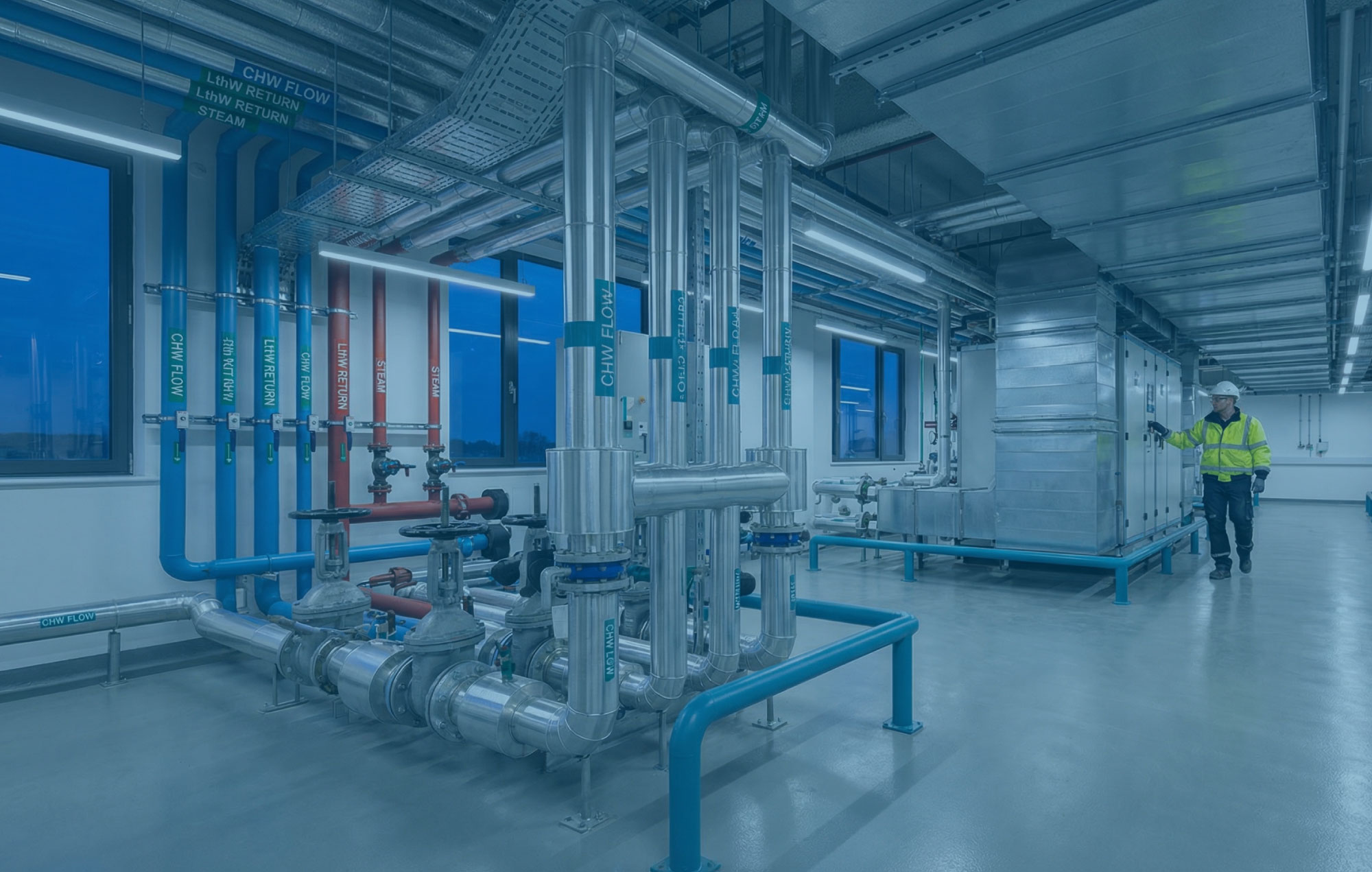 Clinical plant room at blue hour with labelled pipework, AHU ductwork and clean floors ready for commissioning