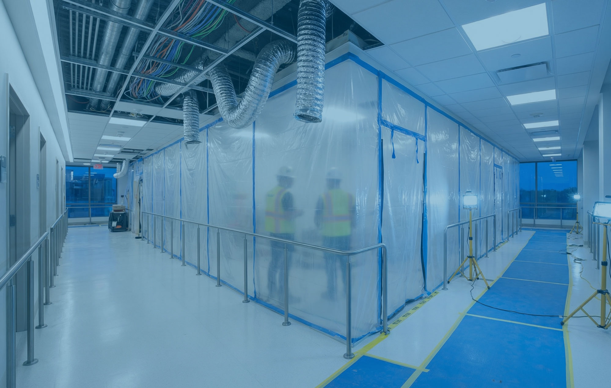 Hospital corridor at blue hour with sealed MEP work zone, temporary services and a clear protected route